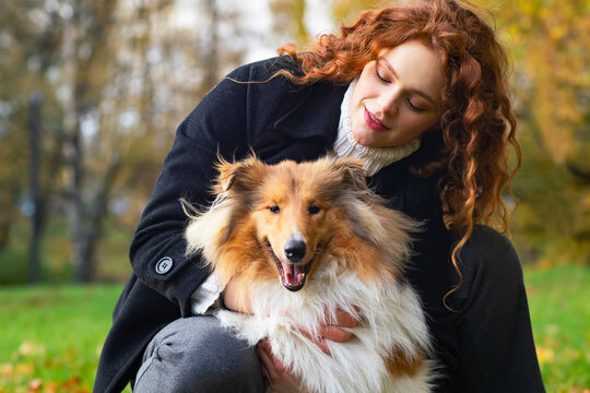 Pretty woman with red hair hugging her collie dog. Female In an autumn park outdoors, pet.