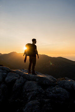 Vertical image of hiker at the top of a mountain enjoying the beautiful golden hour sunset with intense color and blue sky fused with yellow, carrying a large backpack