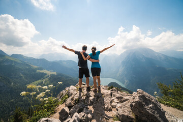 Girl and boy standing on the top of a cliff holding each other and spreading arms, beautiful scenery in the background - Powered by Adobe