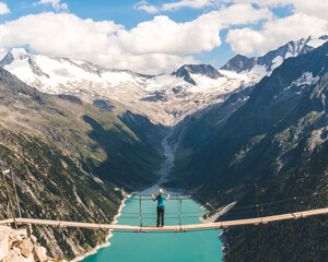 Girl in blue tshirt and a yellow hat sitting on a suspension bridge above the Alps. Freedom and...