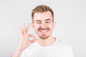 Positive funny male in white shirt shows ok sign, laughs at camera, demonstrates that everything is fine