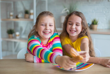 Teen girls together play and eat cakes in the kitchen. Happy kids concept