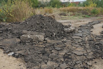 a pile of gray and black pieces of old asphalt on the street near grass and vegetation