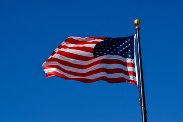 United States Flag flying in the wind on gold brass topped silver Flagpole in white red and blue Stars and Stripes.
