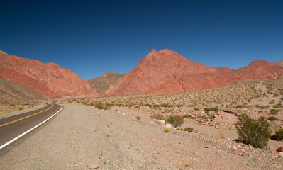 Journey into the wild. Traveling along the asphalt road curve across the arid desert and valley. The empty highway, sand, sandstone and rocky hills under a deep blue sky.
