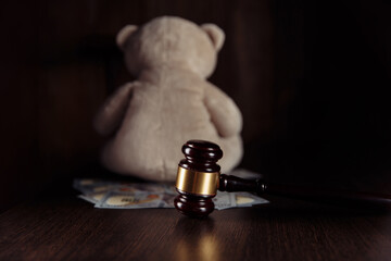 Dollar banknotes, judge gavel and teddy bear on a wooden table. Divorce and alimony concept.