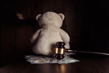 Alimony payment. Dollar banknotes, judge gavel and teddy bear on a wooden table. Divorce, separation and alimony concept.