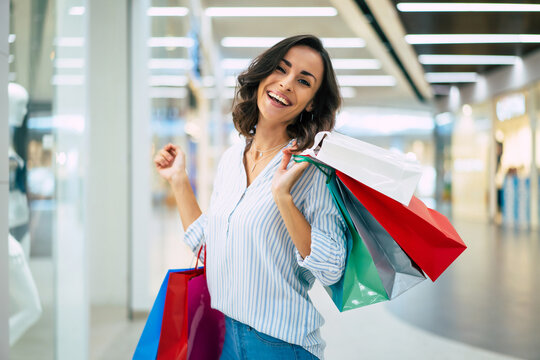 Stylish beautiful young modern woman in trendy clothes with colorful shopping bags is walking on the mall during the buying process