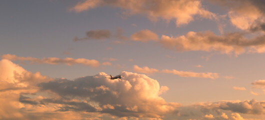 Flying airplane with bright big clouds in sunset colors