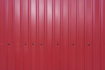 Fragment of a wall made of red profiled metal sheet. Black hexagonal screw heads are available. Background. Texture.
