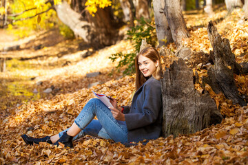 Young girl draws in the album while sitting in the autumn park