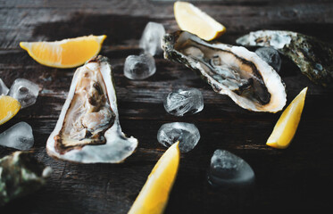 Close-up of fresh open raw oysters with lemon and ice on a wooden background. Healthy seafood. View...