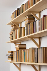 Light wooden bookshelves with hardback overturned books in white interior, home library