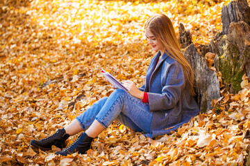 Young girl draws in the album while sitting in the autumn park