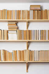 Light wooden bookshelves with hardback overturned books in white interior, home library