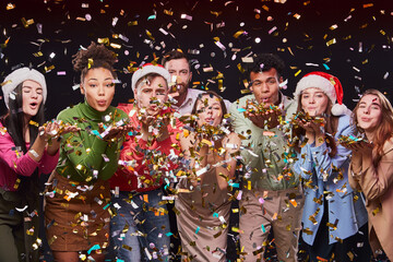 Obraz na płótnie Canvas Celebrating New Year 2021 together. Group of young multiracial happy people blowing colorful confetti