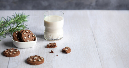 Crispy round cocoa cookies and a glass of milk on a white rustic wooden table
