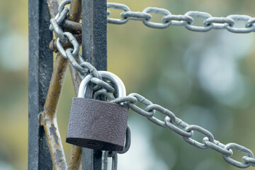 The metal gates is locked with a padlock. The iron chain is wrapped around a fence.
