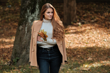 Obraz premium Girl in a brown raincoat with long black hair in the autumn park.