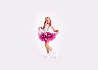 portrait of a cute girl in bright multicolored clothes and with colored braids and in a skirt shows dance exercises on a white background