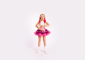 portrait of a cute girl in bright multicolored clothes and with colored braids and in a skirt shows dance exercises on a white background