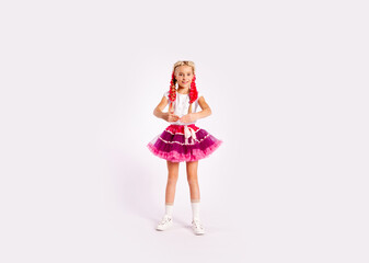 portrait of a cute girl in bright multicolored clothes and with colored braids and in a skirt shows dance exercises on a white background