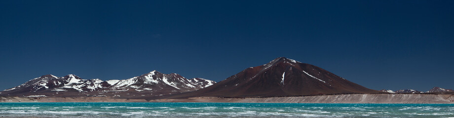 Volcanic landscape in the Andes mountain range. Panorama view of the turquoise color water lake called Green Lake, the dark mountains with snowy peaks and volcanoes, high in the cordillera.