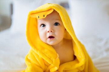 Baby wearing yellow bathrobe duck on parents bed after bath - obrazy, fototapety, plakaty