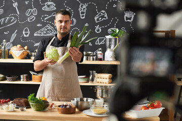 Portrait of professional chef holding fresh vegetables and telling about them to the camera for his...