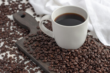 White cup of coffee and coffee beans on dark cutting board