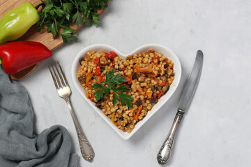 Homemade pasta ptitim with vegetables on heart-shaped plate on gray table. Top view. Horizontal...
