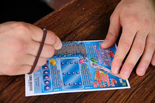 Hand of young man in movement scratching a romanian lottery ticket on busy cafe table. Sighet, Romania, July 21 2019