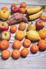 Many orange and yellow autumn fruits like apples, mandarins, pears and bananas on a wooden table