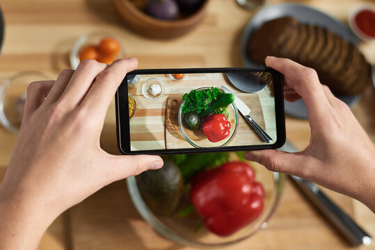 Close-up of female hands holding mobile phone and making photo of fresh vegetables in bowl