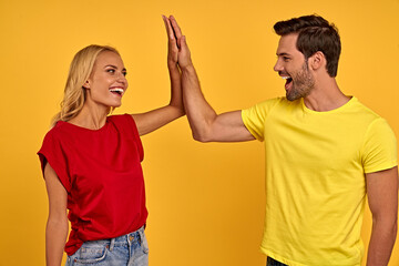 Smiling young couple friends guy girl in t-shirts isolated on yellow wall background studio portrait. People lifestyle concept. Mock up copy space. Looking at each other, giving high five.