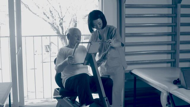 Nurse helping elderly man with legs machine at gym. Sepia toned