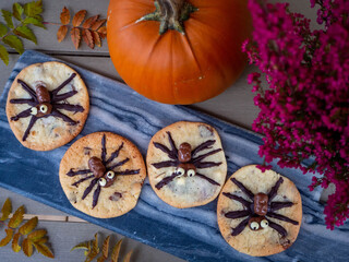 Homemade spider chocolate chip cookies on a dark marble plate. Pumpkin and fall flowers and leaves.