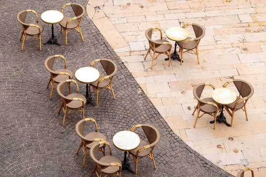 An empty outdoor french cafe with white tables and rattan chairs seen early morning from above, in the city of Nimes. Vertical view