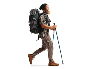 Full length profile shot of a bearded man with a backpack and hiking poles walking