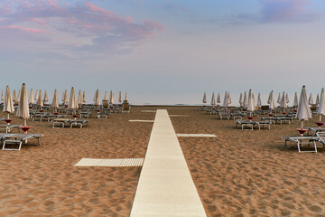 Sunbeds and umbrellas closed in the deserted beach at the end of summer season in Caorle, the small Venice.
