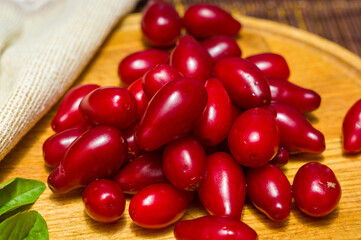 Still life - fresh large dogwood berries, purple plums and a sprig of basil on a wooden board