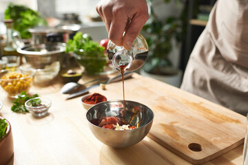 Close-up of chef pouring soy sauce into the bowl he making vegetable salad in the kitchen