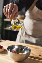 Close-up of chef adding oil into the bowl with salad he making special dish