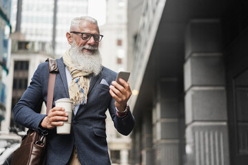 Senior business man using smartphone app walking to work - Entrepreneur drinking coffee while going...