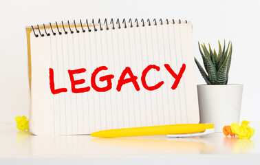 Legacy text, inscription, phrase is written in a notebook that lies on a dark table and a pen.