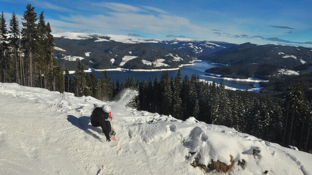 A  Young Man Trying To Jump On A Snowboard But Failing.