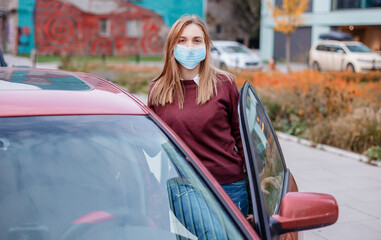The girl gets behind the wheel of a red car. Woman in a medical mask near the car. Girl in a medical mask near the car. coronavirus, disease, infection, quarantine, medical mask, covid-19.