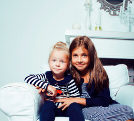 two cute sisters at home playing, little smiling girl in house interior on sofa, messing hair,...