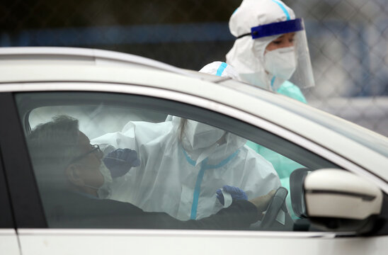 Medical staff member with mask and protective equipment performs Coronavirus nasal swabs test tubes at drive-through testing point in an effort to curb the spread of COVID-19 (novel coronavirus)