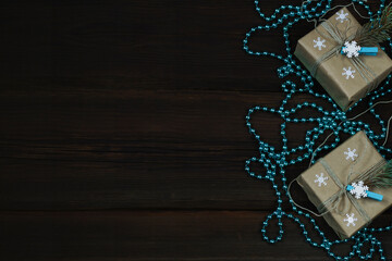 Handmade Christmas gift boxes decorated with craft paper, snowflakes, on a dark wooden background from above. Festive turquoise beads. Card. Winter new year theme. Copy space.